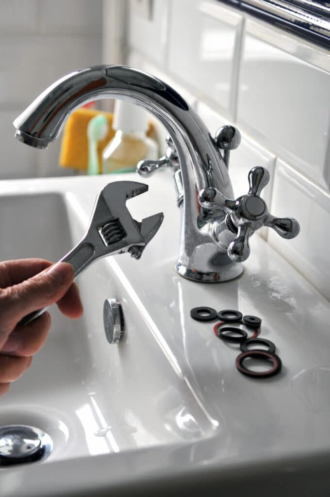 Main tenant une clé à molette près d'un robinet d'évier brillant, avec des joints de rechange, pour une réparation de plomberie.